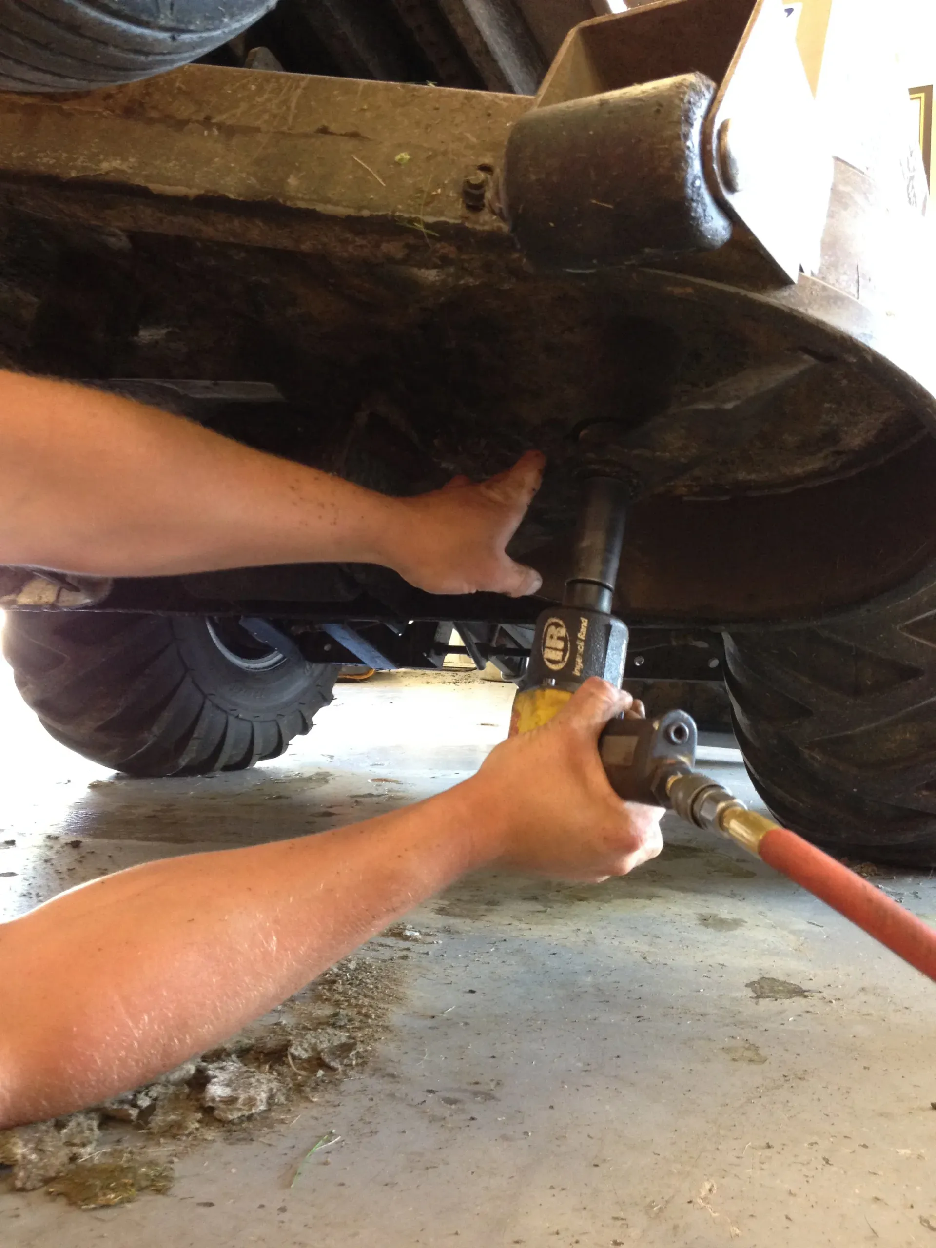 Hands using a pneumatic jack to lift a vehicle, presumably for maintenance or repair, in a garage setting.