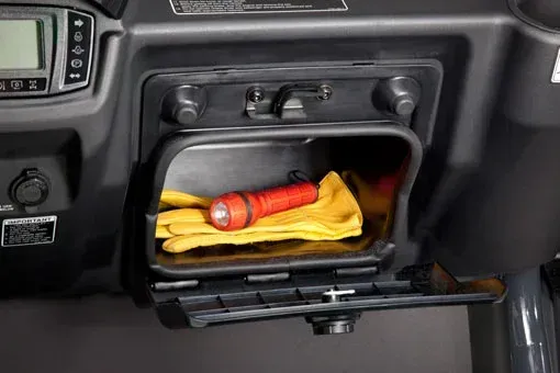 Open storage compartment in a vehicle console containing a flashlight and work gloves. Black and tan interior.