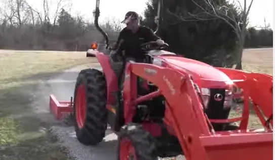 Man driving a red tractor on a gravel path outdoors.