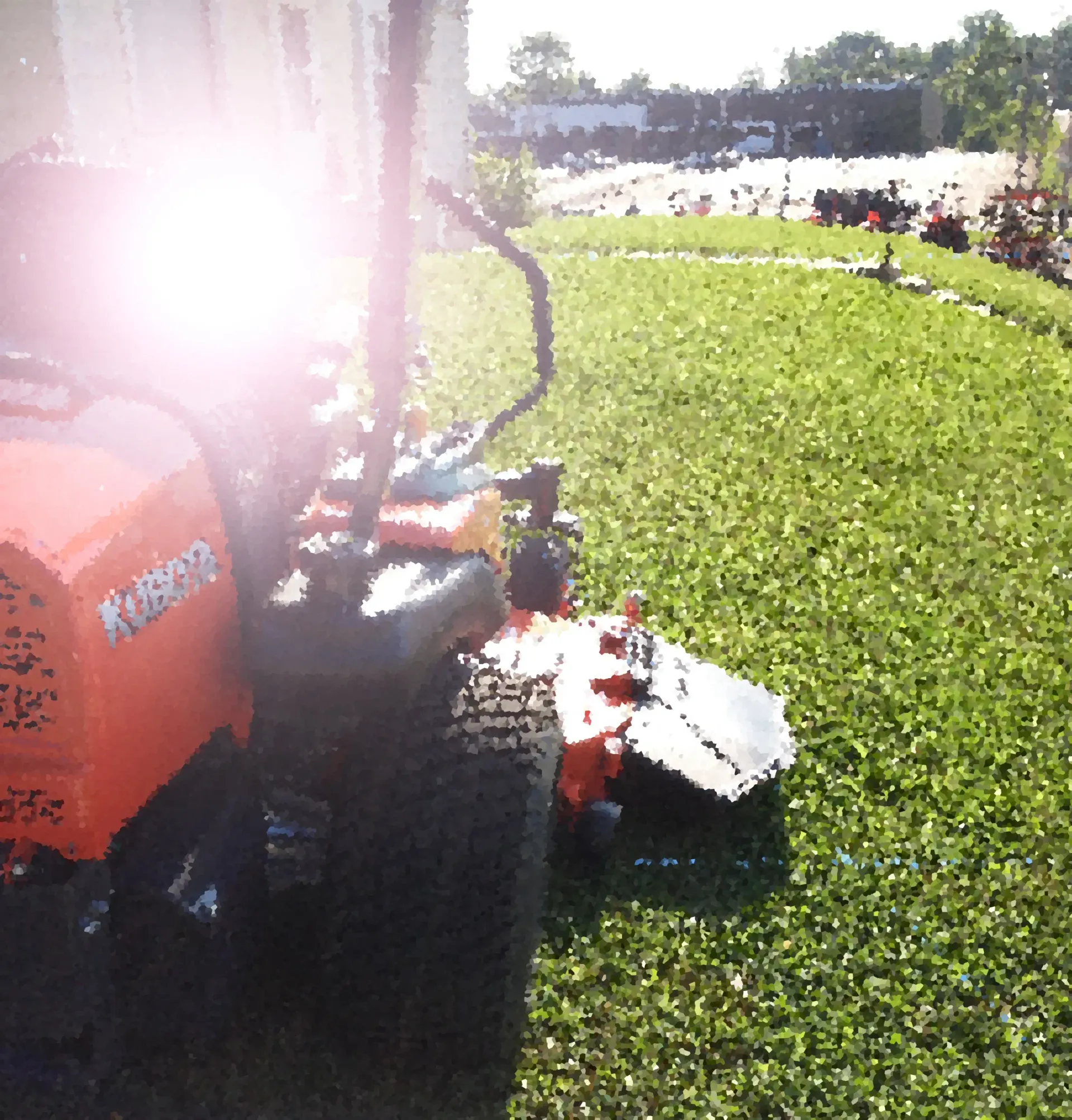 Orange riding lawnmower on a green lawn, bright sun flare.