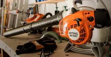 Orange and white Stihl leaf blower on a shelf with gloves and other tools.