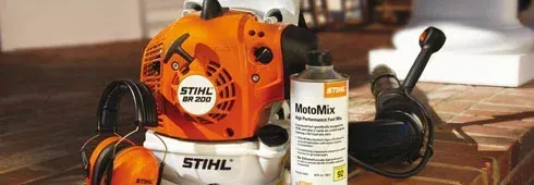 Stihl leaf blower, ear protection, and fuel container. Orange and white. Wooden surface.