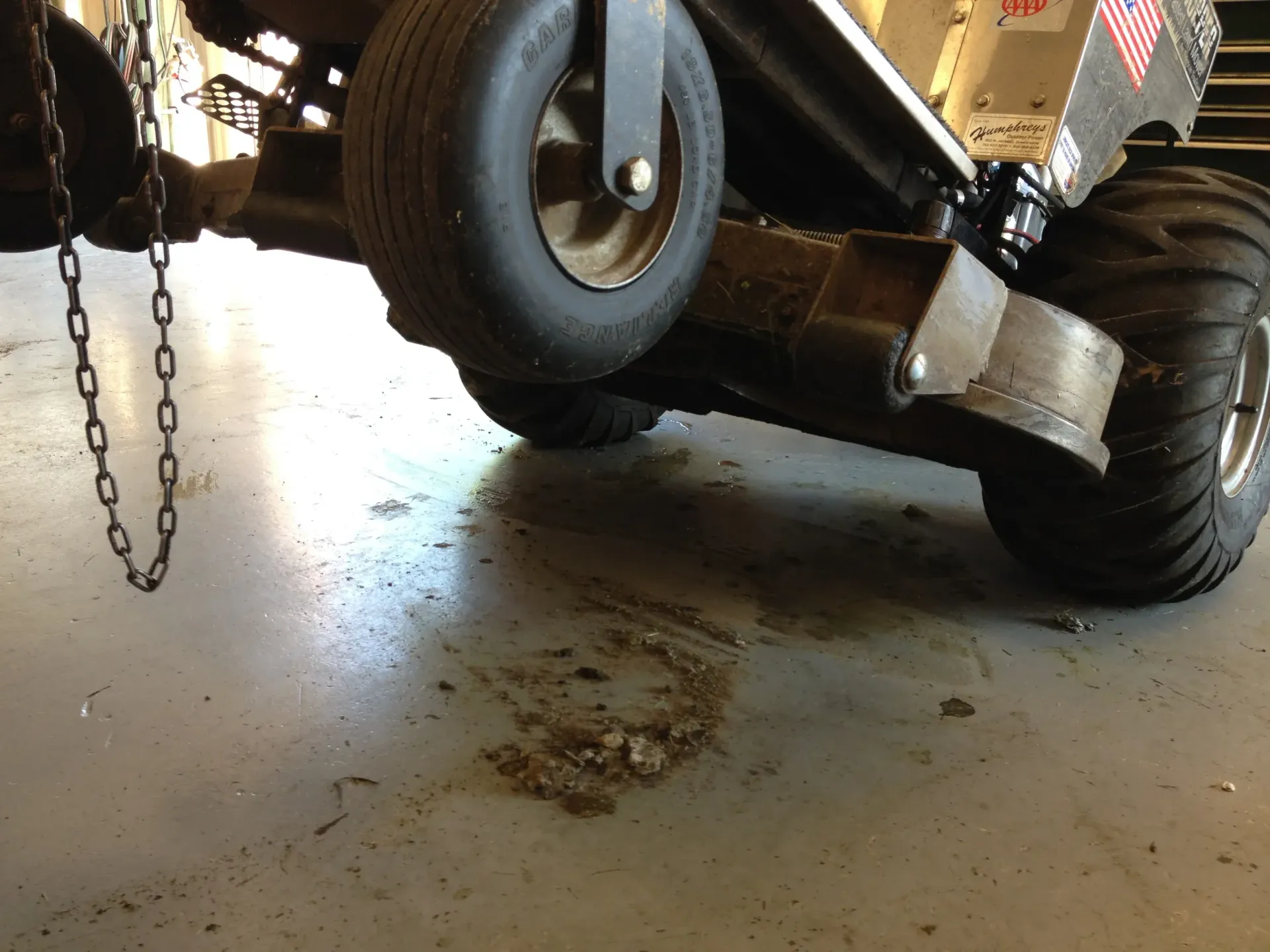 Mower with visible oil spill on concrete floor; chain hanging.