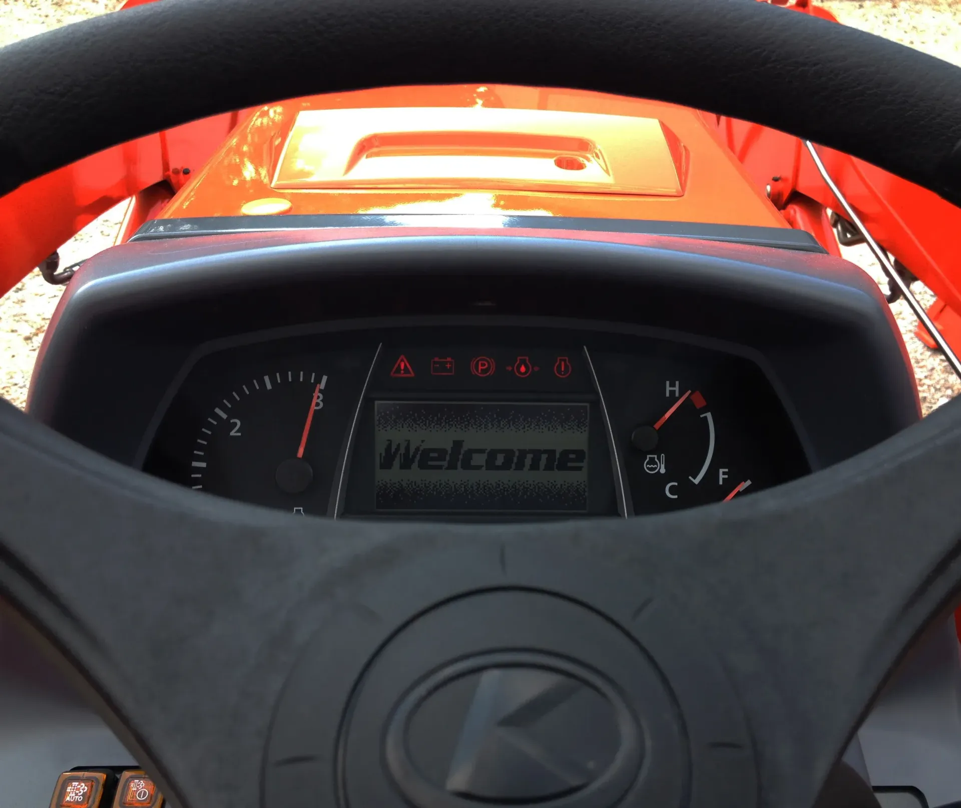 Dashboard of an orange Kubota tractor showing Welcome message, gauges, and warning lights behind the steering wheel.