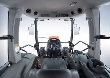 Interior of a tractor cab, view from the driver's seat. Gray and black interior, windshield, and controls visible.