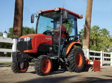 Orange Kubota tractor with enclosed cab, operating on a dirt area.