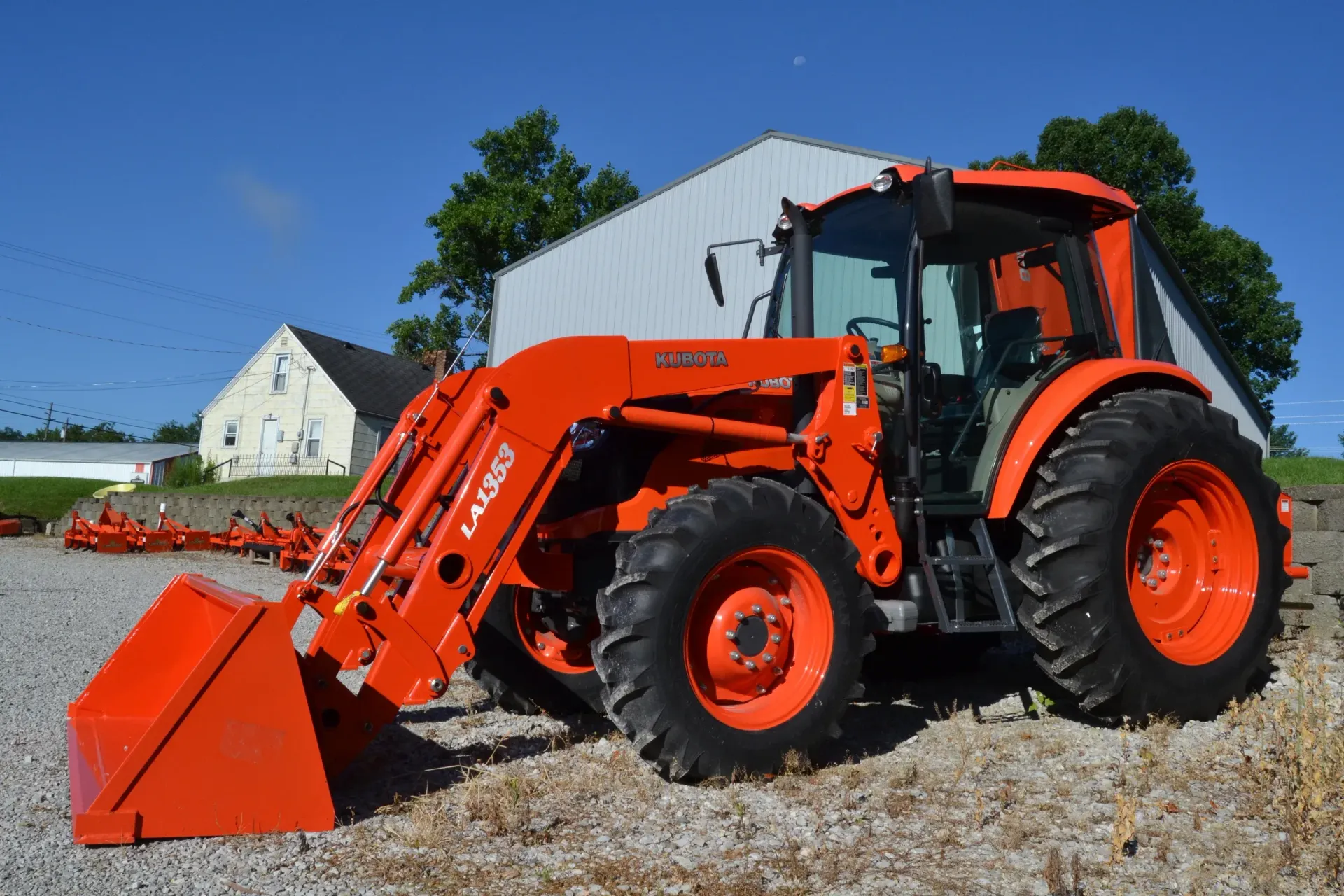 Orange tractor with front loader parked outdoors in front of a white building.