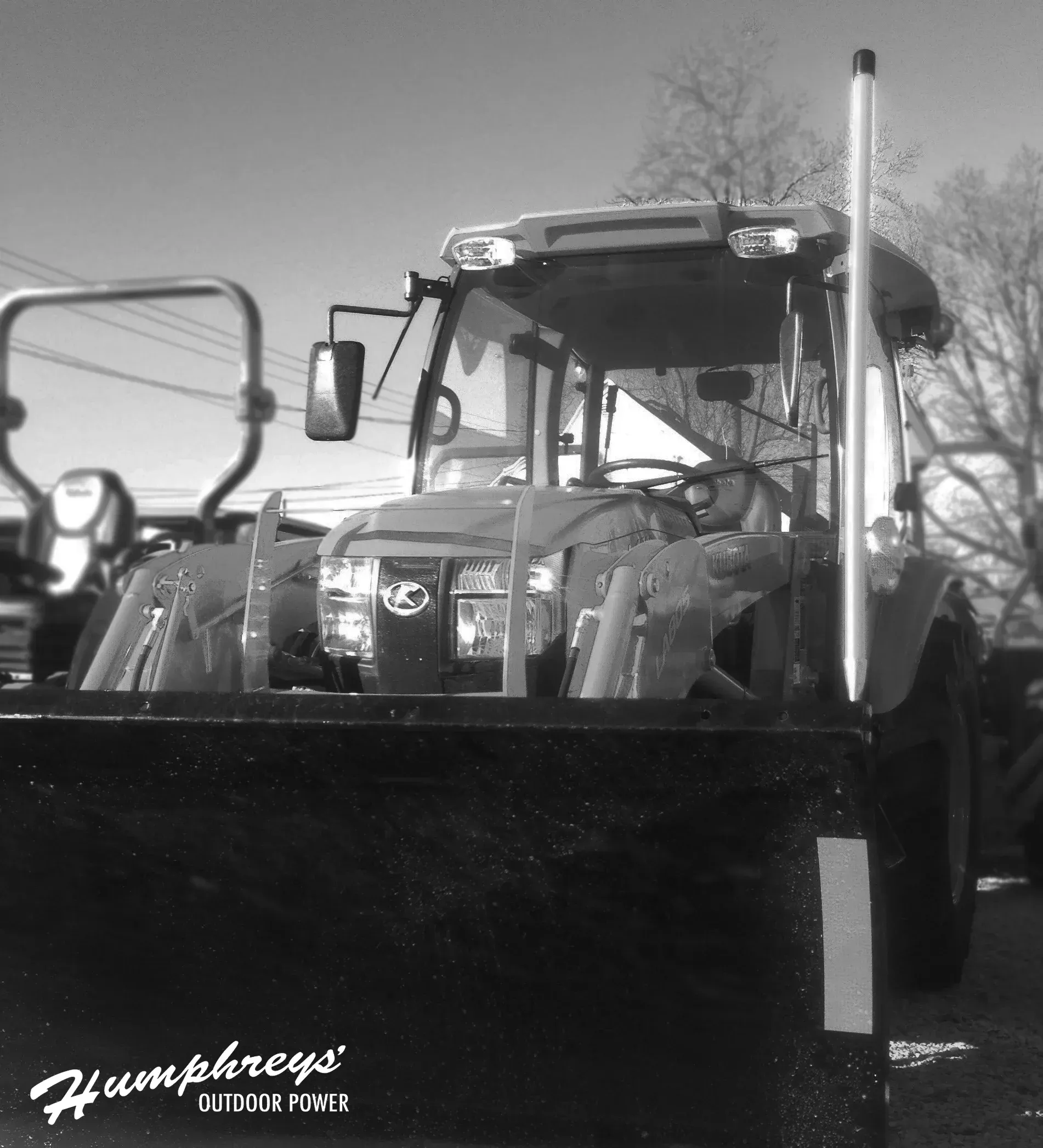 Black and white image of a tractor with a front loader, parked outdoors on a sunny day.
