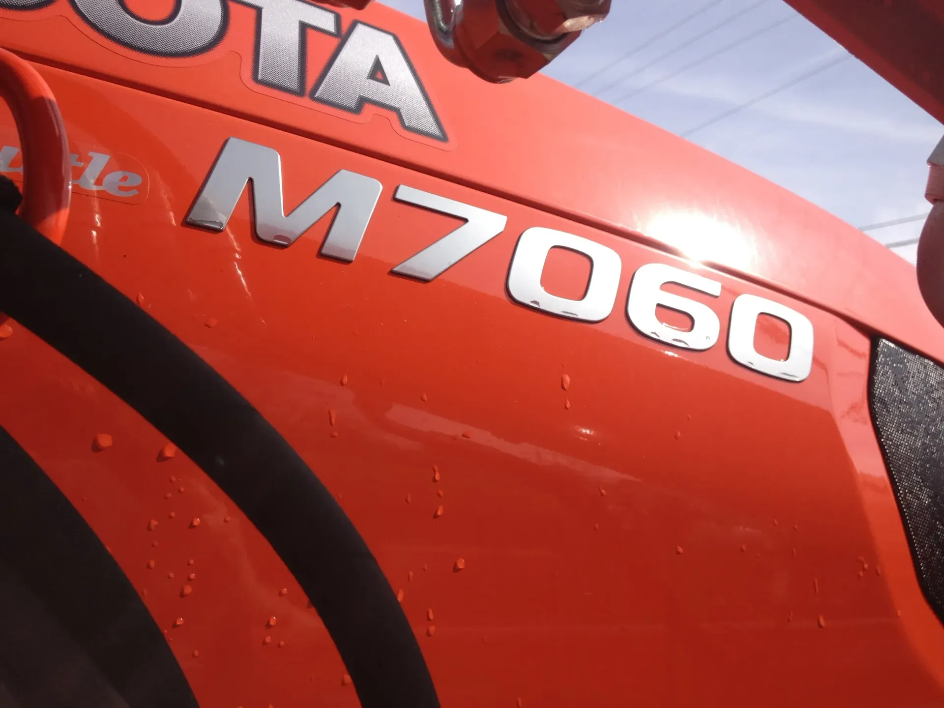 Orange Kubota M7060 tractor side, with black tire visible.
