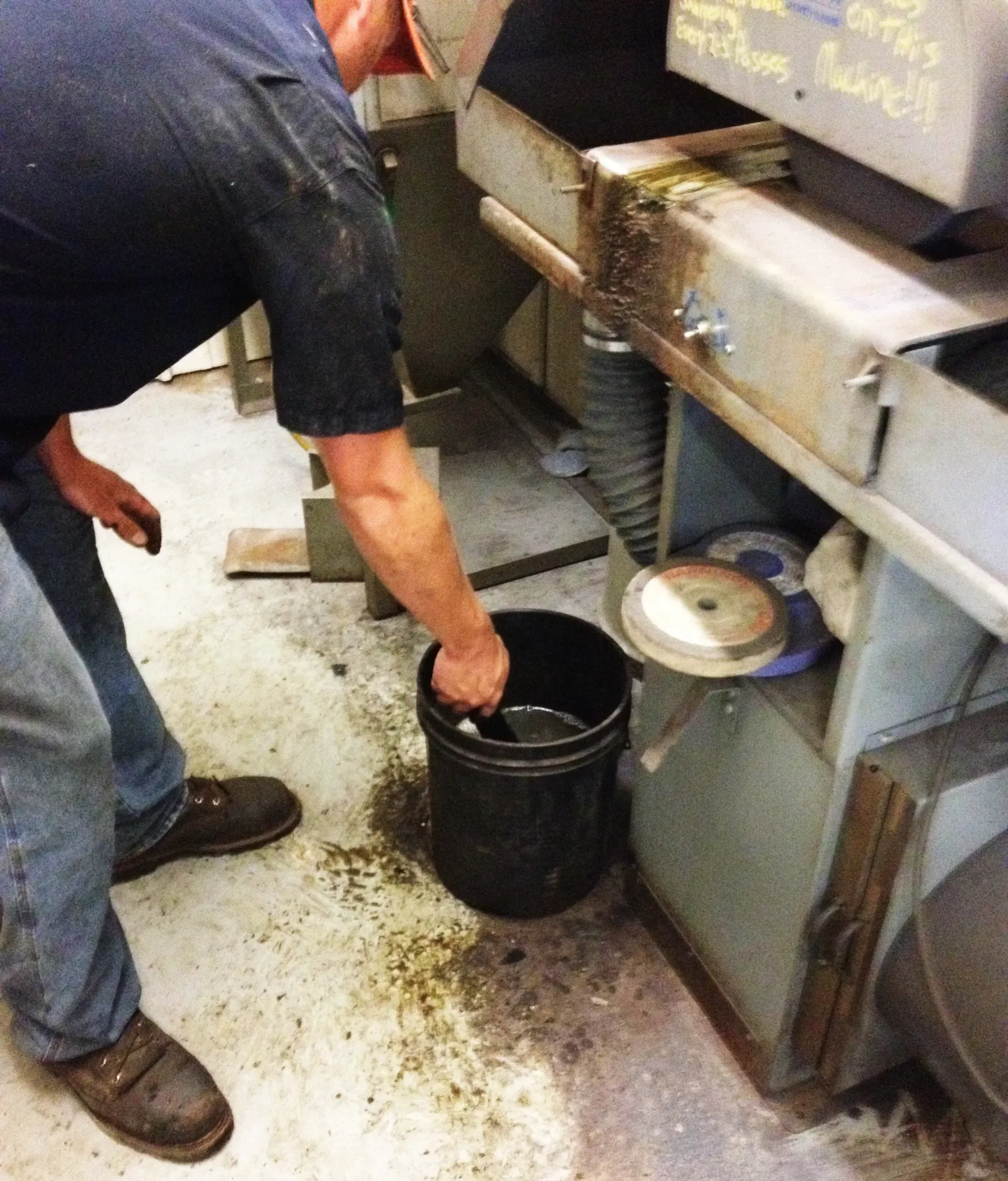 Man near machinery, dipping an object in a dark bucket, likely using coolant in a workshop.