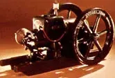 Black vintage stationary engine with flywheel on wooden base.
