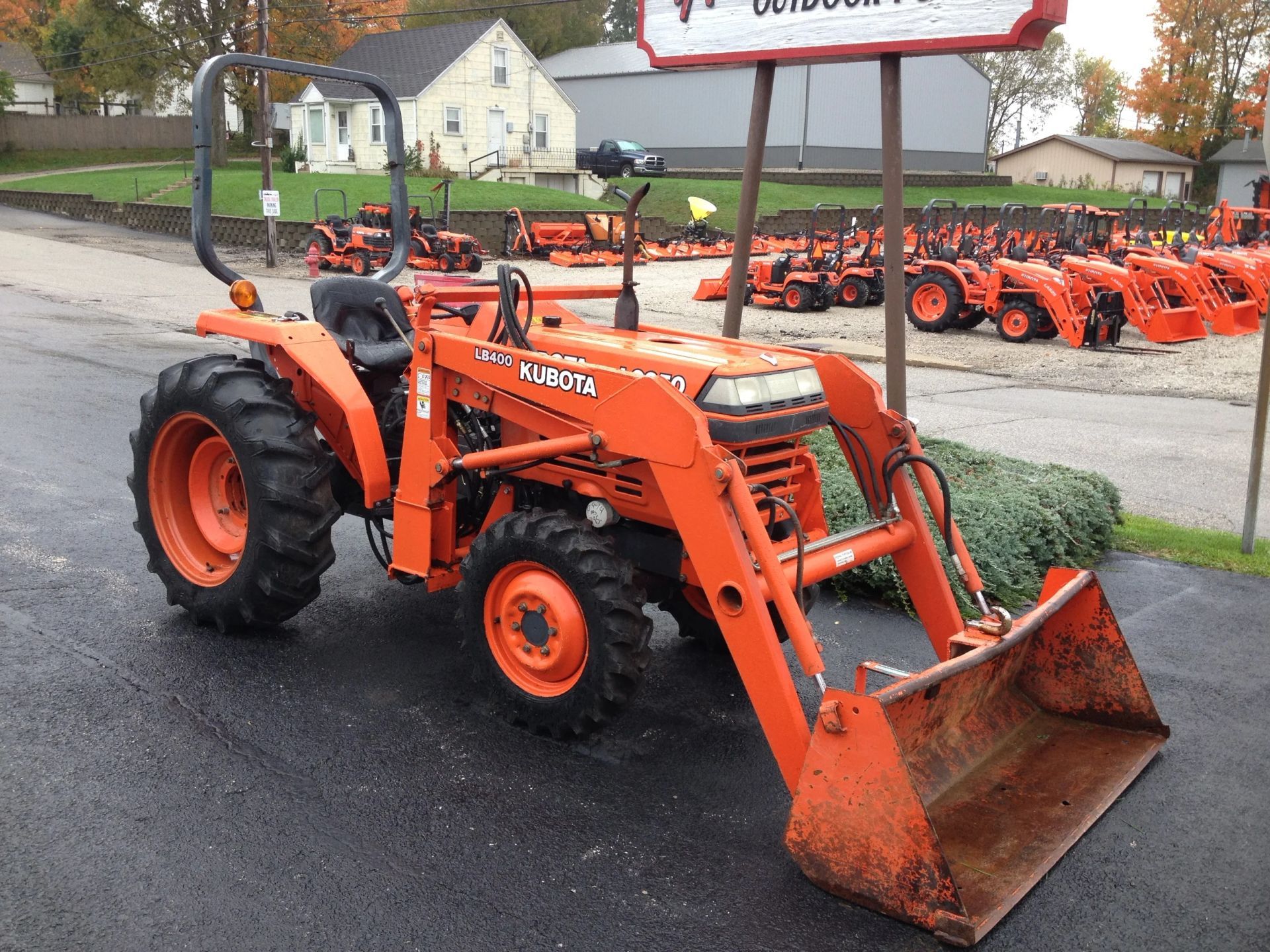Orange Kubota tractor with front loader parked on asphalt. Other tractors are in the background.