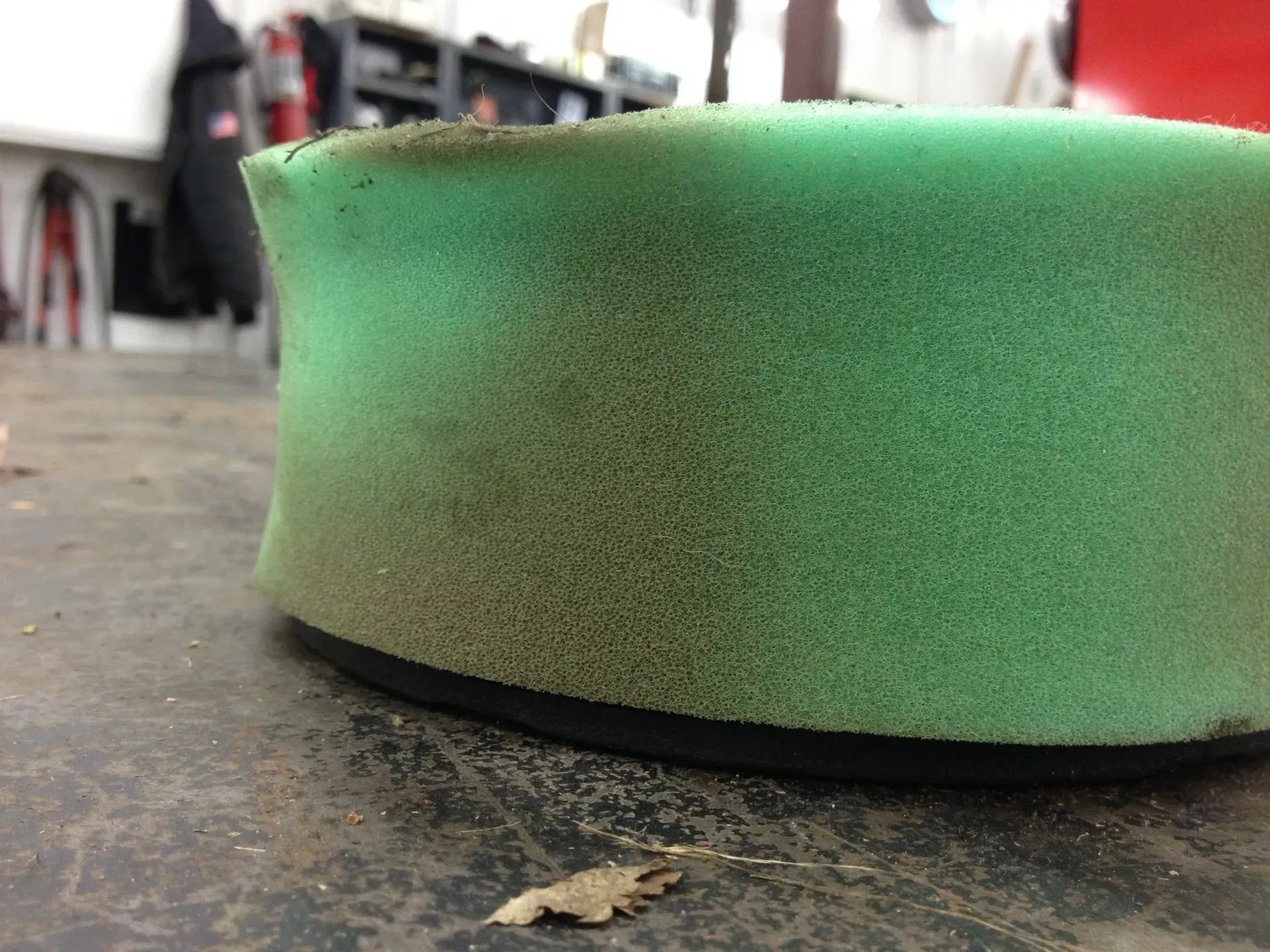 Green foam air filter, dirty with dark debris, on a work surface.