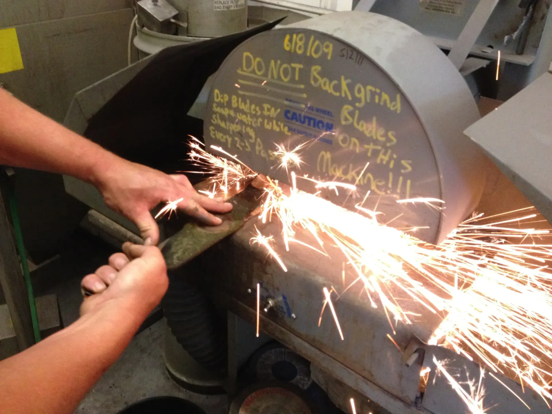 Hands sharpening a blade on a grinding wheel, sparks flying.