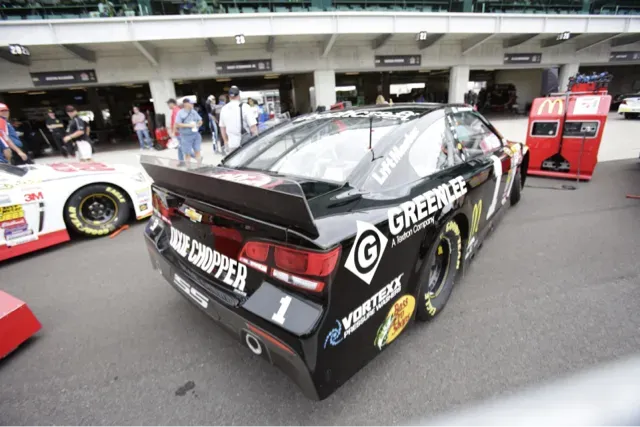 Black and white stock car with sponsor logos parked in a pit garage.