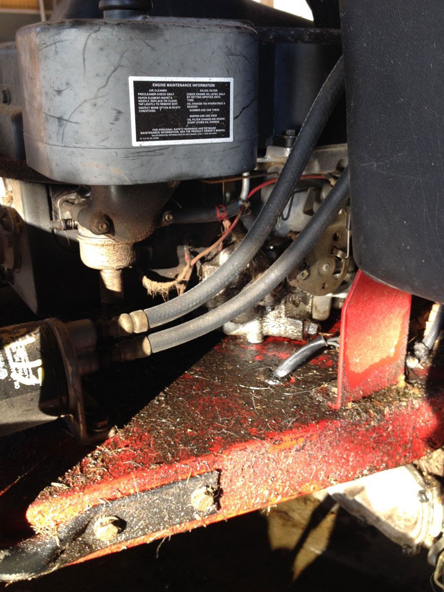 Close-up of a machine's engine and surrounding parts. The frame is red and covered in debris.