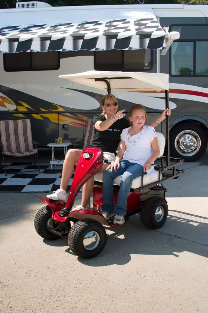 Woman and girl in red golf cart with awning, parked in front of RV.