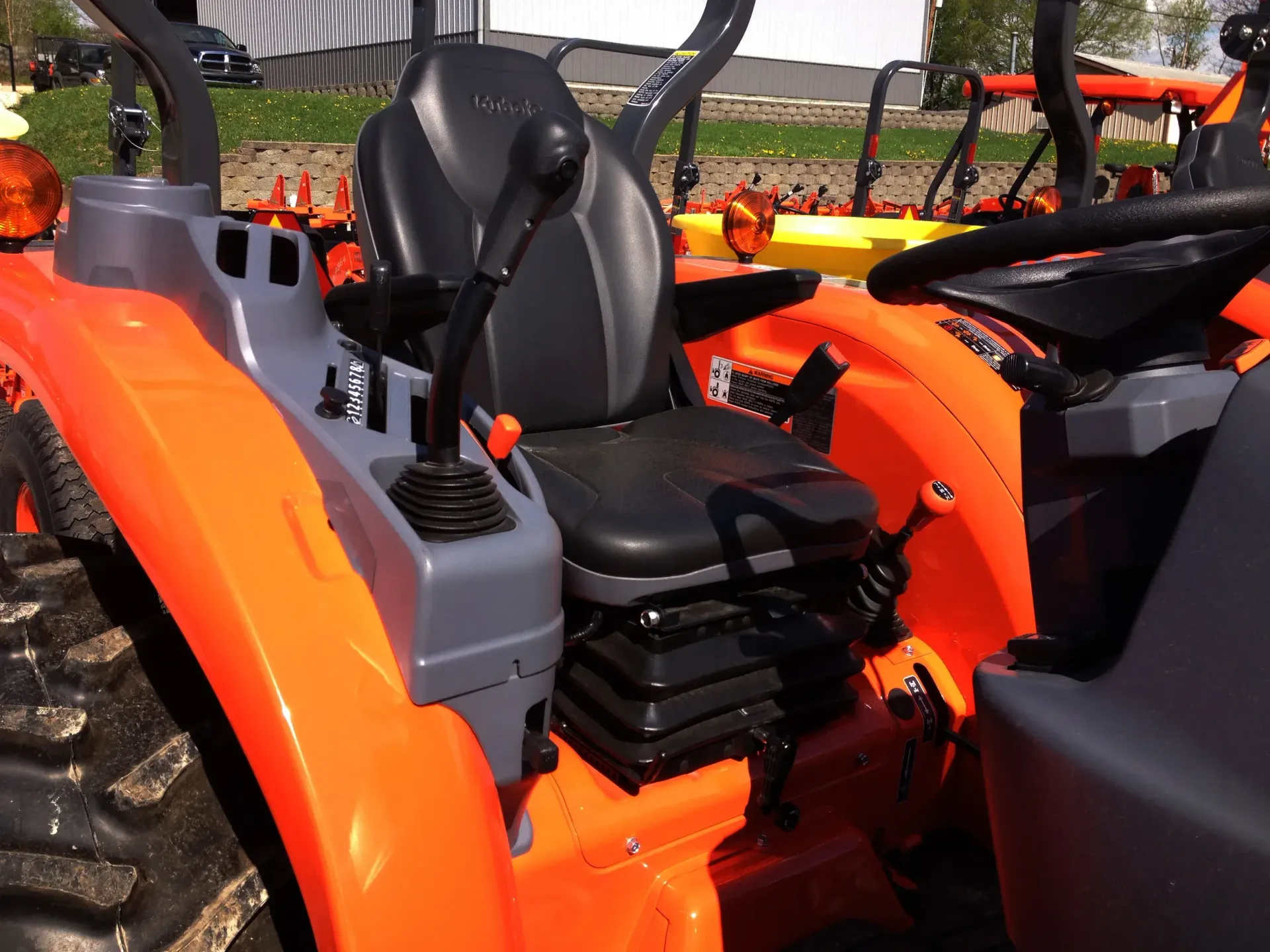 Orange tractor's operator's station: gray control panel with levers, black seat. Sunny outdoor setting.