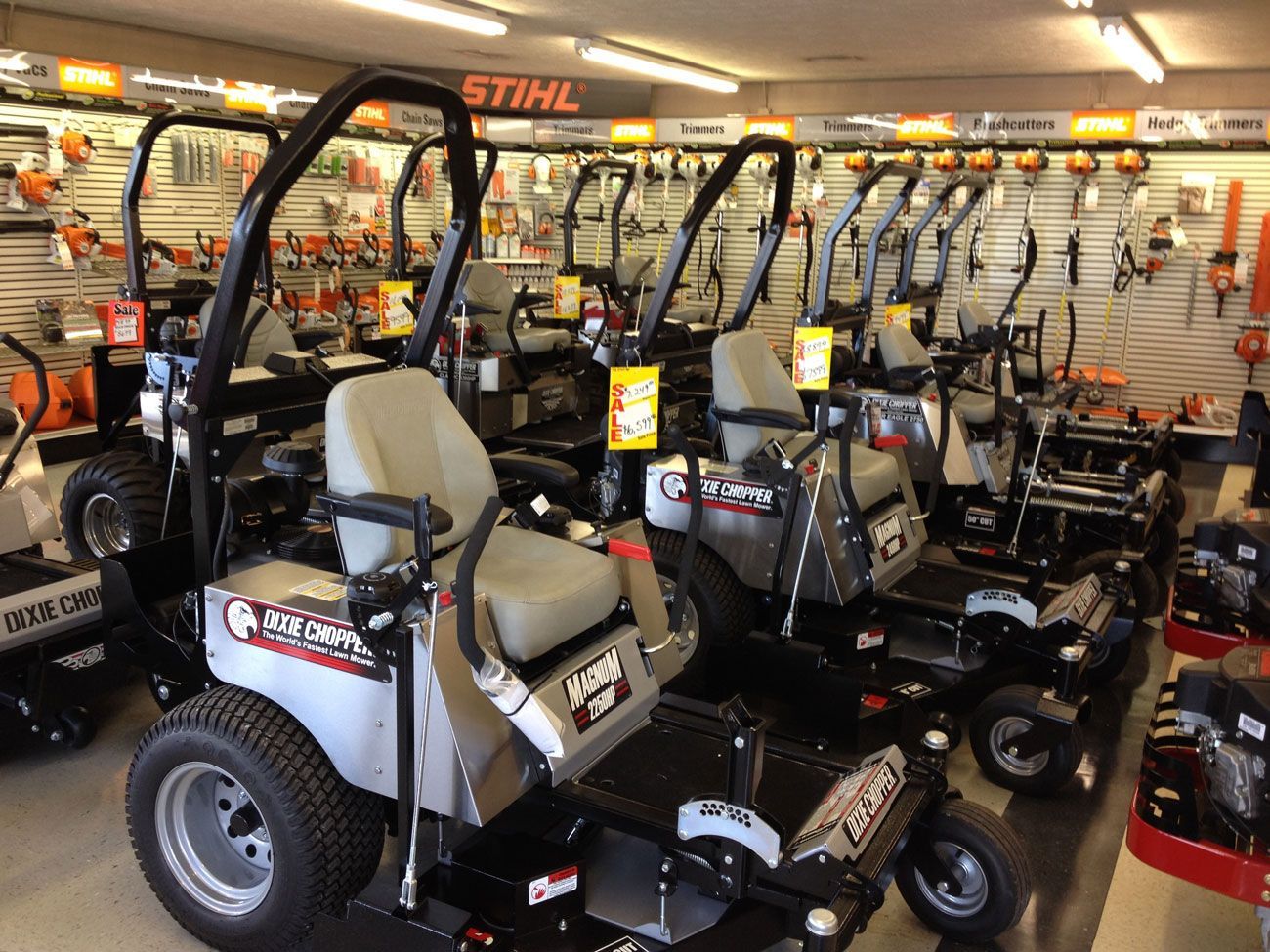 Row of zero-turn mowers inside a store; tools and equipment on the back wall.