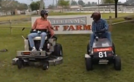 Two people on lawnmowers wearing helmets.