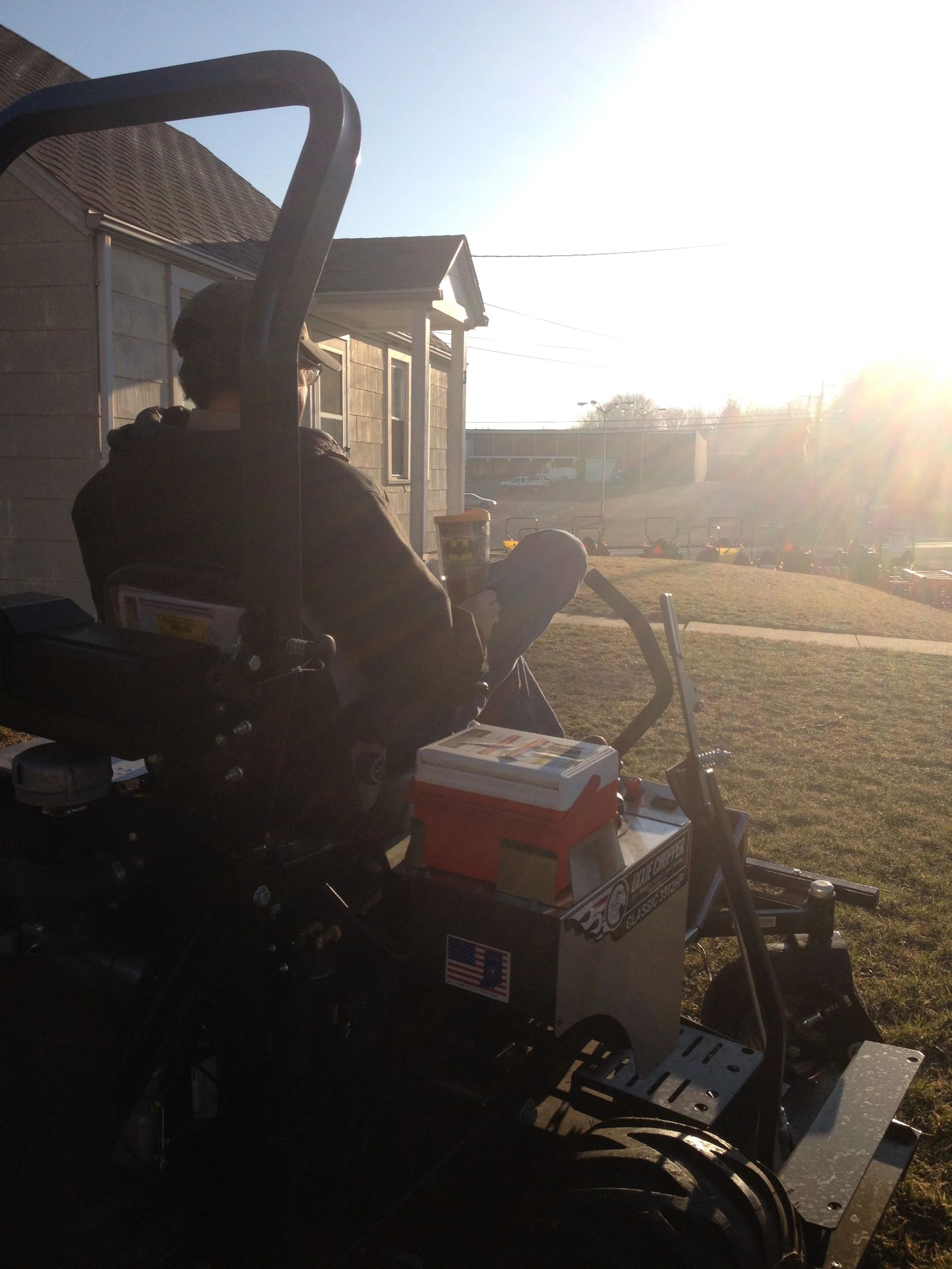 Person on a riding lawnmower on a sunny day near a house.