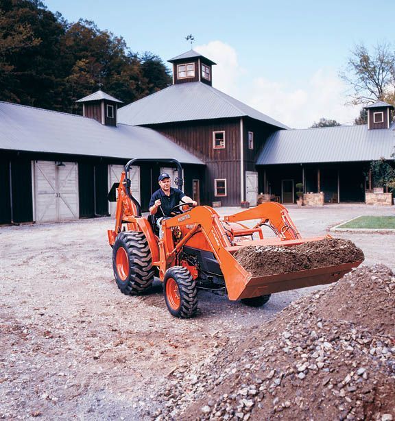 Orange tractor with dirt in the front bucket, in front of a barn.