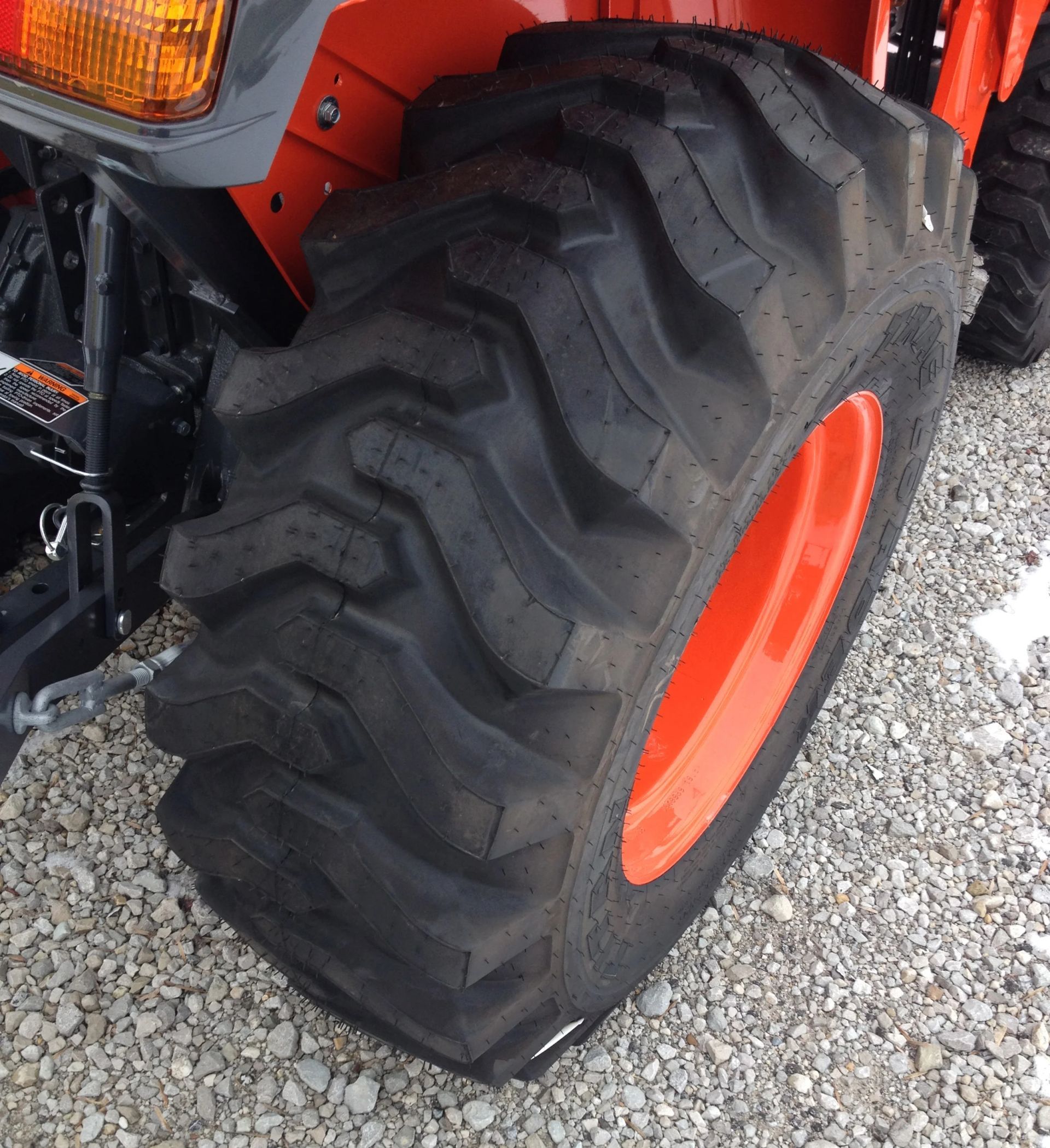 Orange tractor tire with black tread, side view.