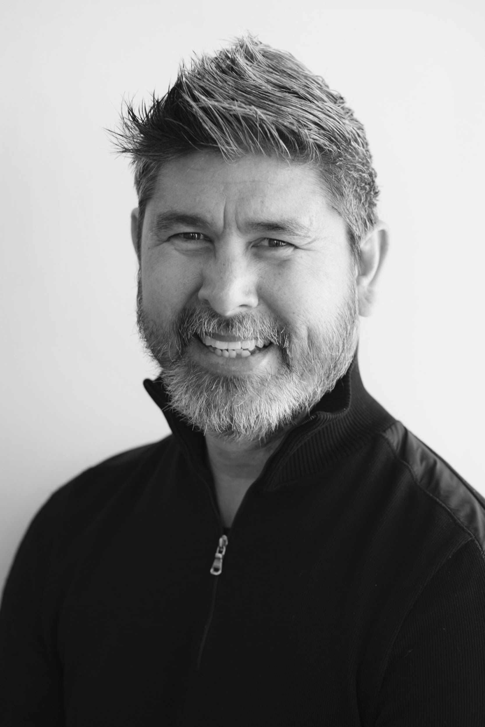 A man with a beard is smiling in a black and white photo.