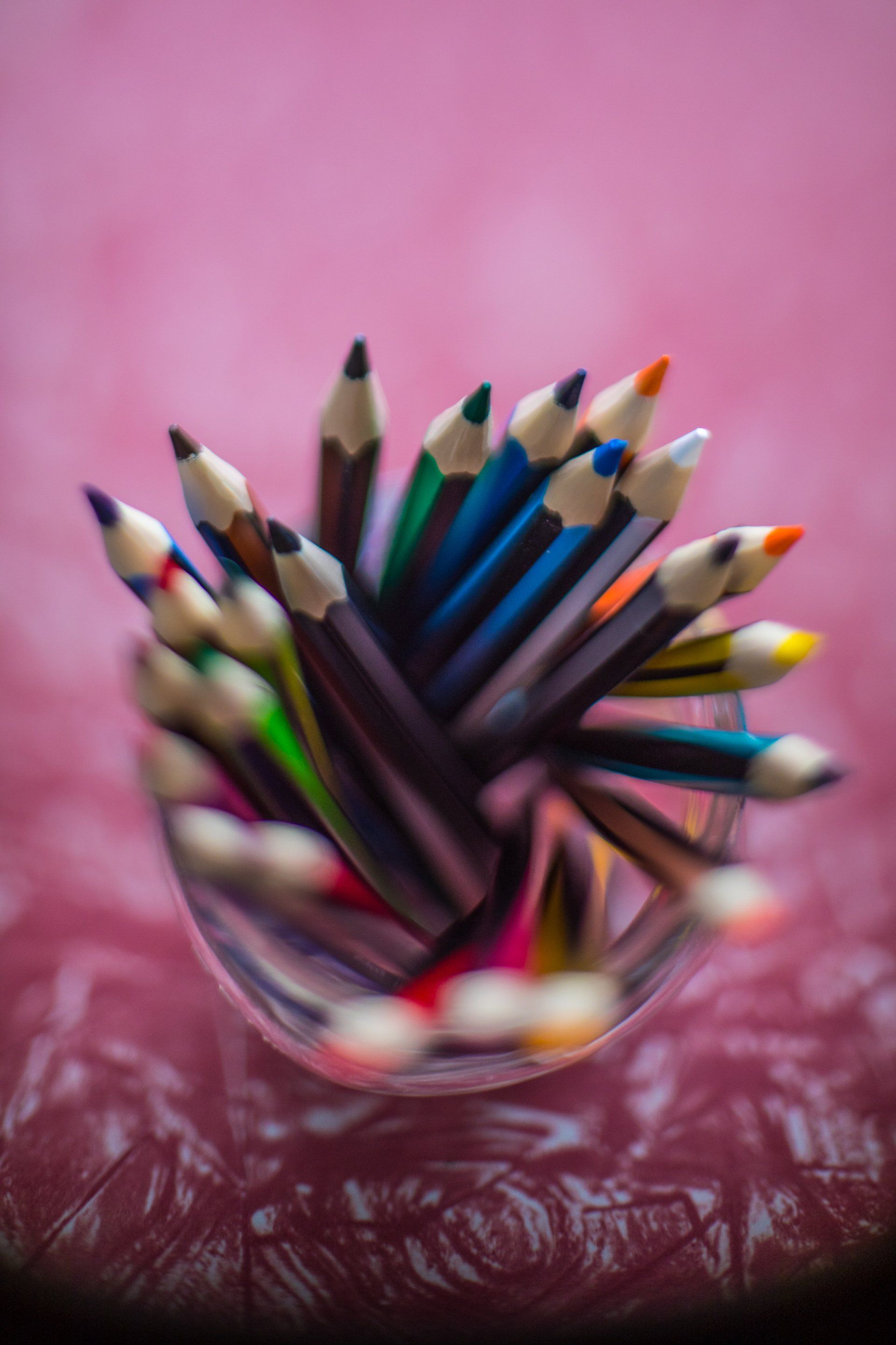 A glass filled with colored pencils on a pink background