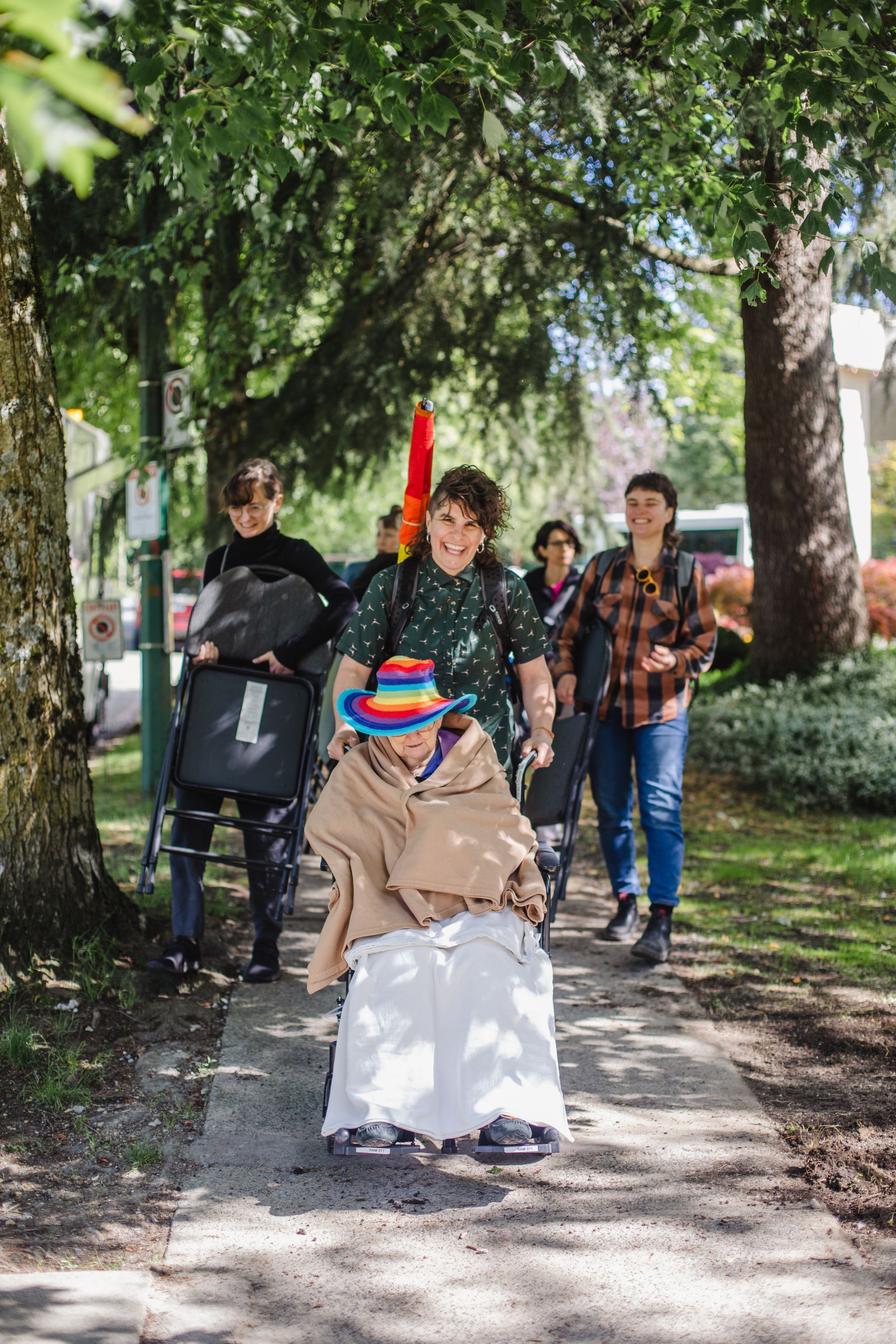 A group of people are walking down a sidewalk with an elderly woman in a wheelchair.