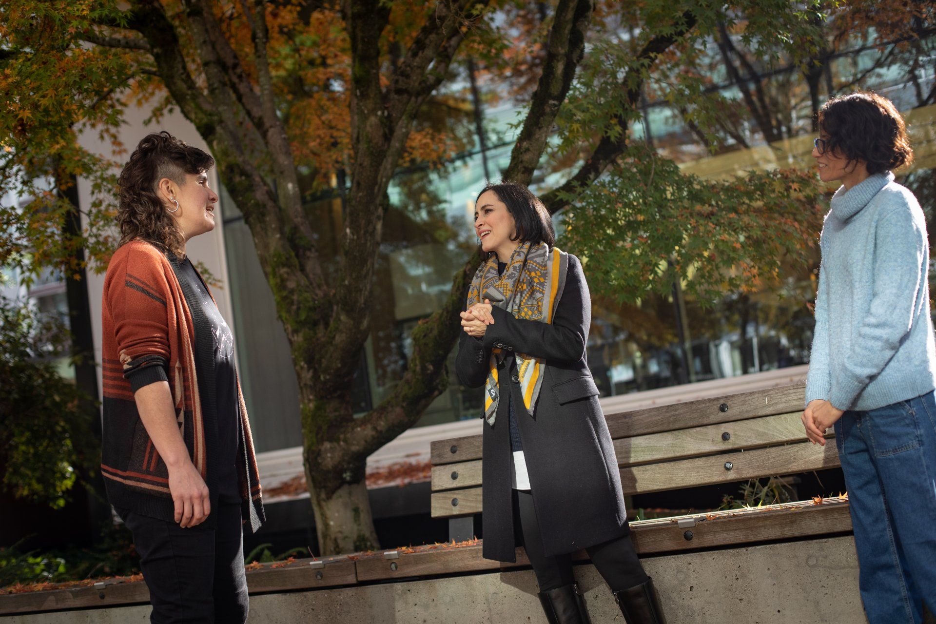 Three individuals are standing next to each other in front of a tree.