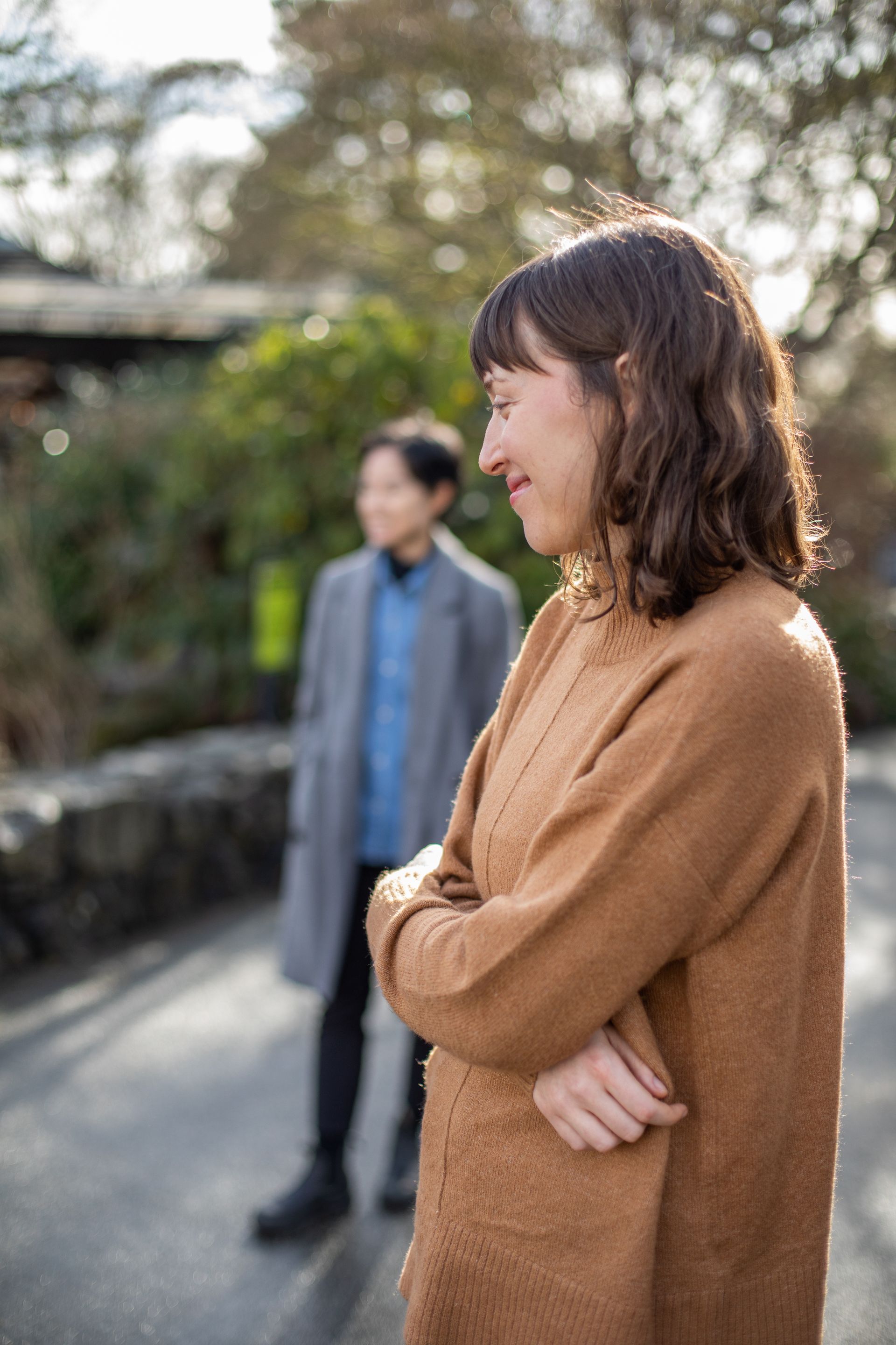 A person in a brown coat is standing next to a person in a grey coat.