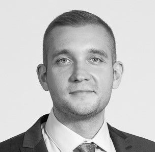 Man in suit and glasses looking to the side with a slight smirk.