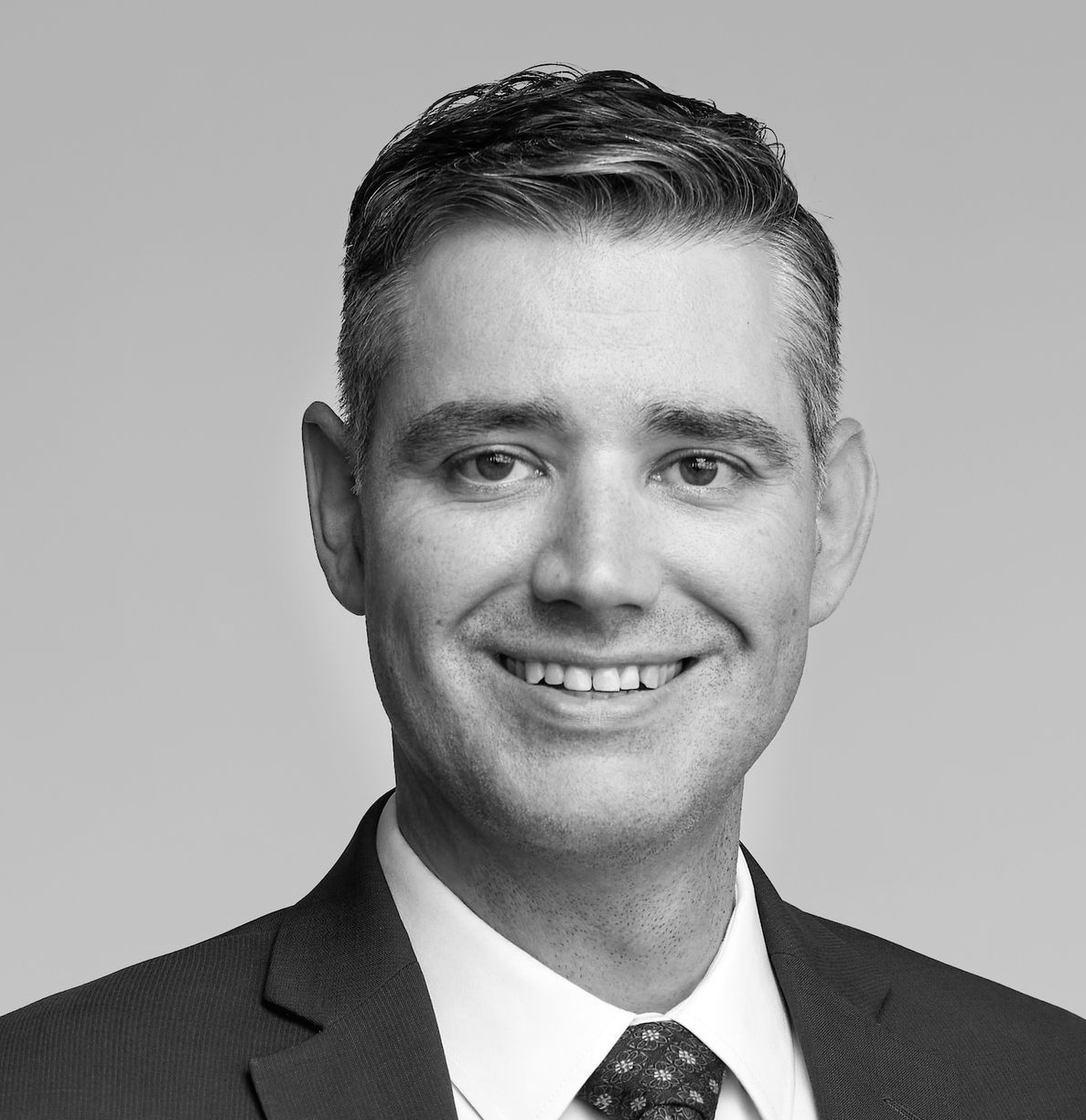 Man in suit and glasses looking to the side with a slight smirk.