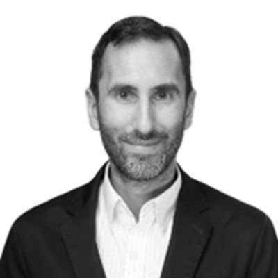 Man in a dark suit jacket, white shirt, and short beard, smiling slightly.