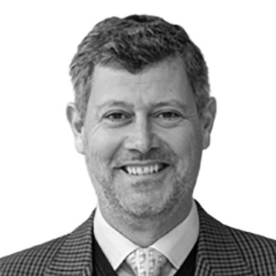 Man smiling, wearing a tweed jacket and tie, headshot.