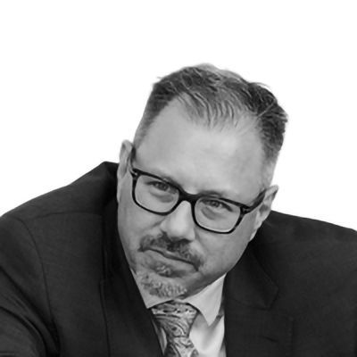 Man in suit and glasses looking to the side with a slight smirk.