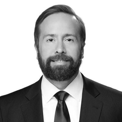 Man in a suit, tie, and full beard, smiling slightly, against a white background.