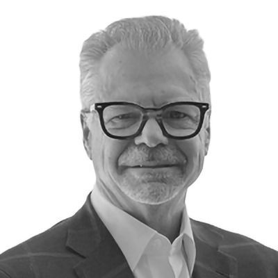 Man wearing glasses and a suit, smiling.