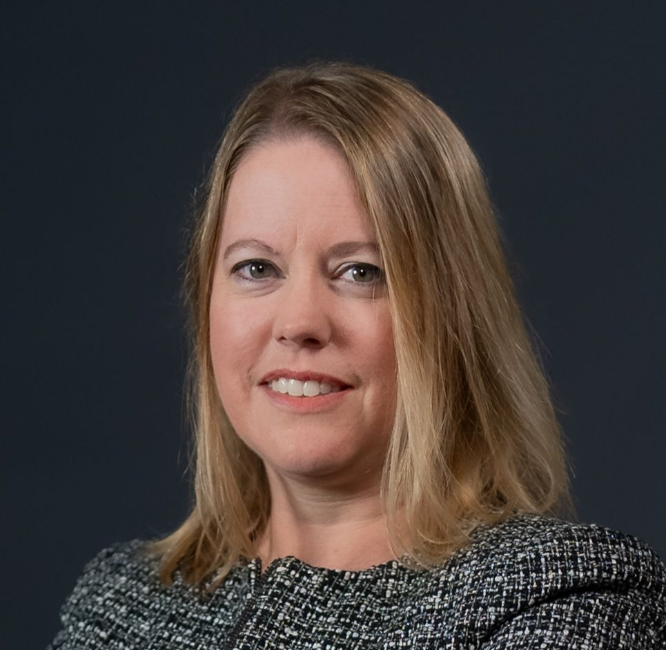 Man in a light purple dress shirt, smiling, against a white background.