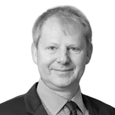 Man in a suit smiles, headshot against a white background.