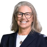Woman wearing glasses smiles at the camera, wearing a blazer and white shirt.