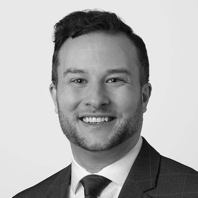Man in suit and glasses looking to the side with a slight smirk.