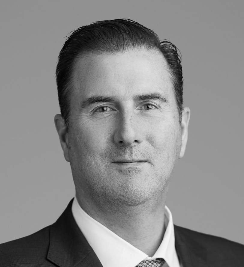 Man in suit and glasses looking to the side with a slight smirk.