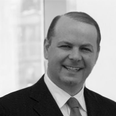 Man in suit smiling, indoors, with a window in the background.