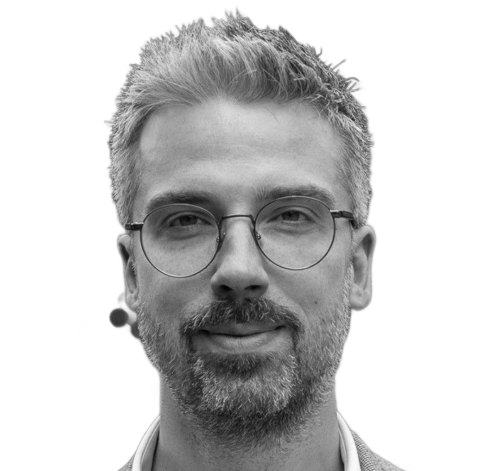 Man in suit and glasses looking to the side with a slight smirk.