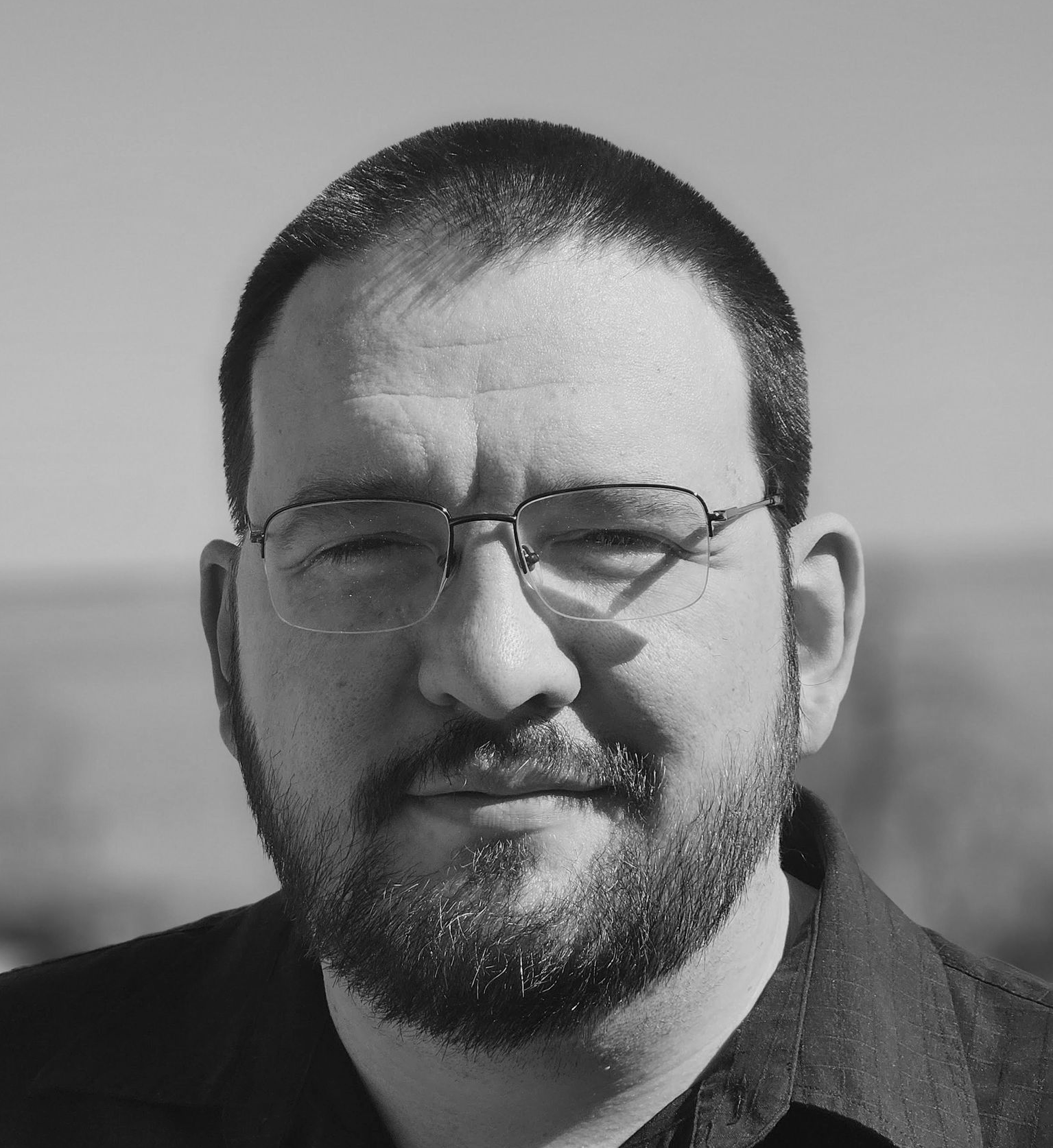 Man in suit and glasses looking to the side with a slight smirk.