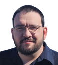 A person with a dark beard and glasses looking directly at the camera against a plain white background.