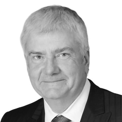 A man in a suit, with gray hair, smiles at the camera. Black and white headshot.