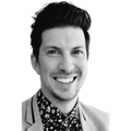 A portrait of a person with dark hair, wearing a dark turtleneck and a textured jacket, against a white background.